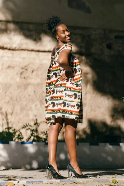 Afro woman posing in dress with ethnic textures smiling at the camera outdoors — Stock Fotó