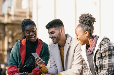 Three friends of different ethnicities looking at the mobile outdoors