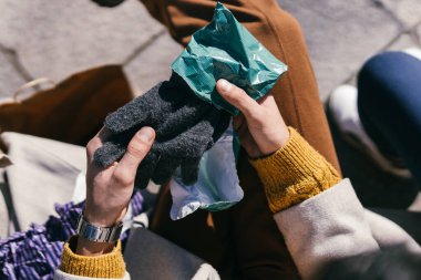 Man holding a pair of woolen gloves he has just been given sitting on a bench