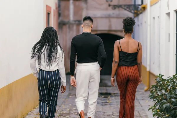 Back of a man and two women in modern clothes walking through a street — 图库照片