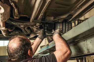 Back of a man under a car fixing steering alignment in a garage