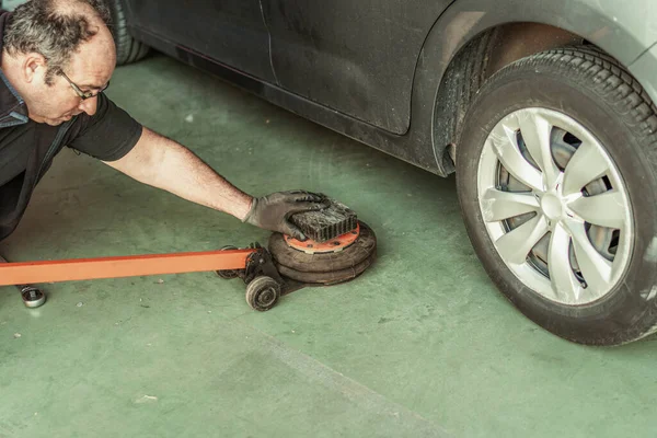 Mechanic putting a jack under a car to lift it into a garage — Foto de Stock