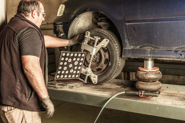 Mechanic checking the operation of a pneumatic jack under a car to lift it — Foto de Stock