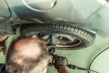 Mechanic putting the screws into a wheel of a car using an electric screwdriver