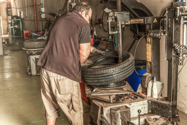 Hombre reparando una rueda en un garaje lleno de herramientas — Foto de Stock
