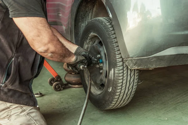 Mechanic using an electric screwdriver to remove a wheel in a garage — Foto de Stock
