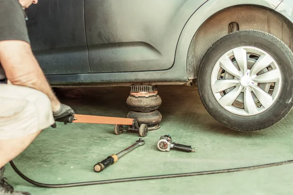 Mecánico usando un gato neumático debajo de un coche para elevarlo a un garaje — Foto de Stock