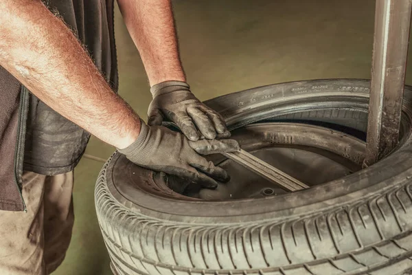 Manos de un hombre reparando un neumático en un garaje sucio — Foto de Stock
