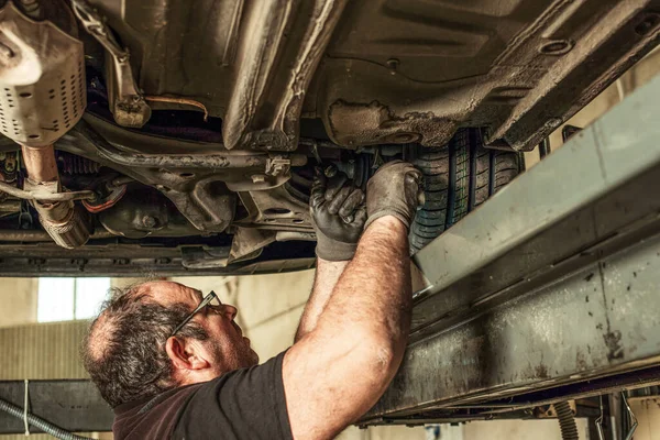 Mecánico sucio en un hueco debajo de un coche que fija la alineación de la dirección en un garaje — Foto de Stock