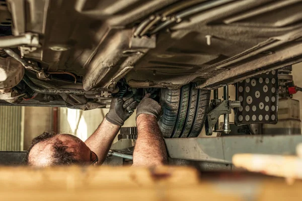 Hombre en un agujero debajo de un coche que fija la alineación de la dirección en un garaje — Foto de Stock