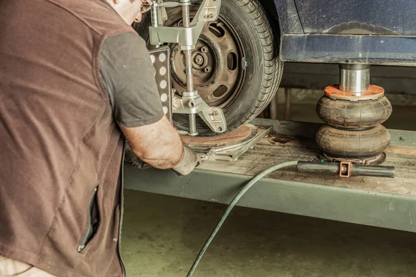 Mechanic aligning the steering of a car lifted by a jack in a garage — Stock Photo, Image
