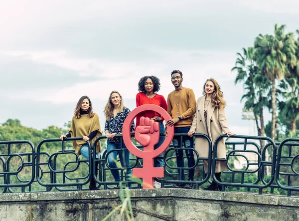 Interracial group of 5 people hold up a feminist cork symbol