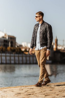 Güneş gözlüklü bir adam nehir kenarında geziniyor. İnsanlar