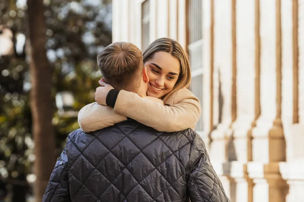 Una giovane donna guarda a terra con un viso felice mentre abbraccia il suo partner — Foto Stock