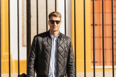 Güneş gözlüklü genç bir adam kameraya bakıp gülümsüyor.