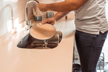 Kirli bulaşıkları lavaboda yıkayan bir adam.