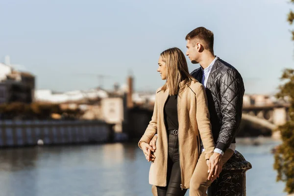 Una coppia che si tiene per mano guardando un fiume in una città — Foto Stock