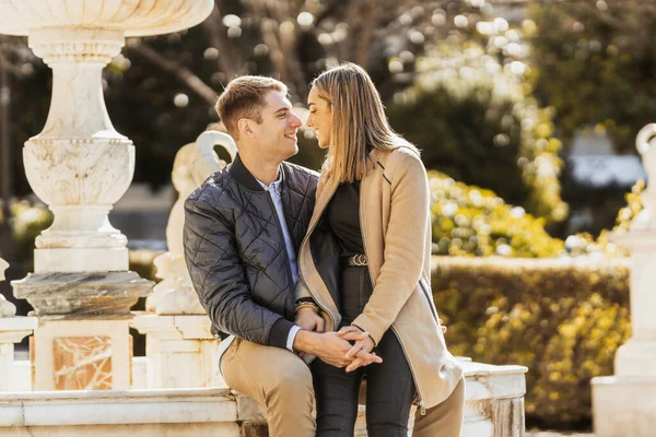 En man som sitter på en fontän och hans flickvän mellan benen ler mot varandra — Stockfoto