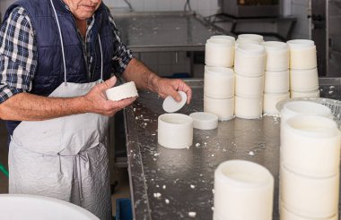 Yaşlı adam taze peynirleri kalıptan çıkarıyor.