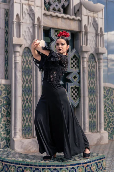Hiszpanka młoda tancerka flamenco ubrana na czarno z czerwoną różą we włosach pozuje na platformie z płytkami z arabską dekoracją — Zdjęcie stockowe