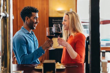 multiethnic couple celebrating with a red wine toast at the bar of a tavern