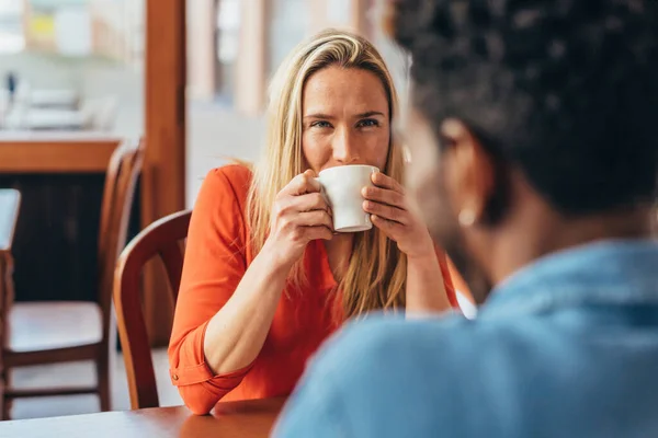 Mujer rubia mira atentamente al compañero negro mientras bebe café — Foto de Stock