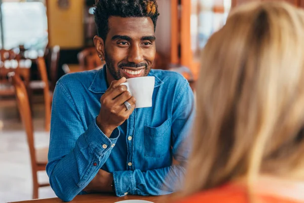 Sonriente hombre afroamericano bebiendo café mientras conversaba con una mujer rubia caucásica — Foto de Stock