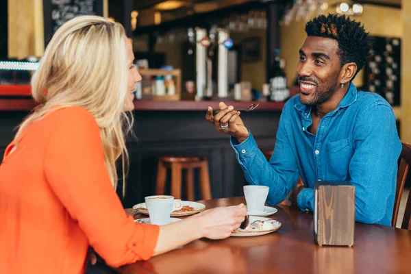Negro hombre beber café y comer chocolate con un caucásico mujer en un restaurante — Foto de Stock