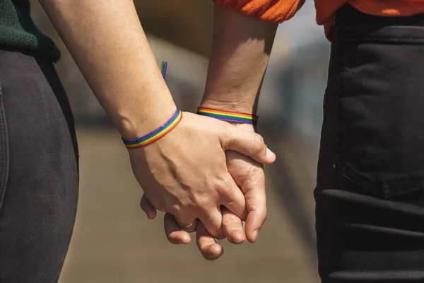 Mãos entrelaçadas de casal lésbico com uma pulseira de arco-íris — Fotografia de Stock