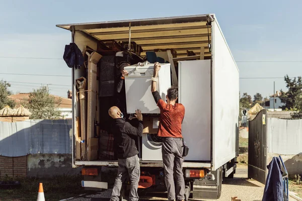 Full shot of 3 colleagues of a moving company load a dishwasher onto the truck