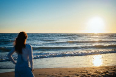 unfocused red-haired woman watches the sunset over the sea