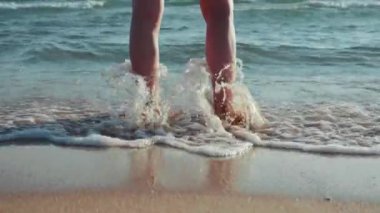 medium shot of a womans feet hit by a small wave on the seashore