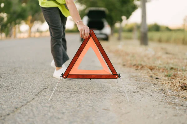 woman setting up the emergency triangle to warn of the presence of a car on the side of the road