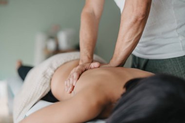 woman rests on a stretcher while a physiotherapist warms up her muscles with his hands. Health