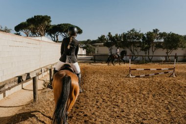 rear view of a woman in equestrian attire warming up a horse by circling the equestrian arena. Ride