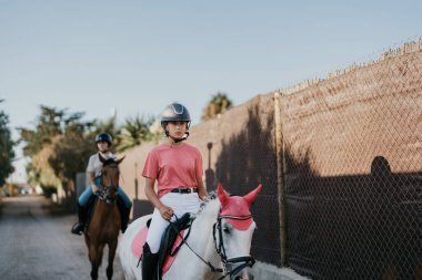 2 young female riders ride their horses through an alleyway. equestrian