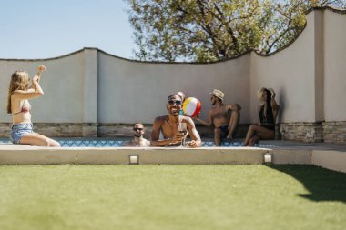 Yüzme havuzunun kenarında elinde bir bardak şarapla gülümseyen siyah bir adamın portresi. Tatiller