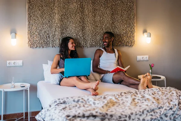 a multiracial married couple smiles in bed while she shows him something on the laptop. Marriage