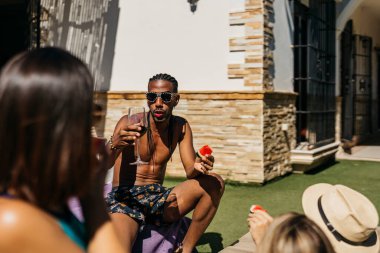 Rasta saçlı, karpuz yiyen ve tatilde arkadaşlarıyla konuşan genç siyahi bir adam. Tatiller