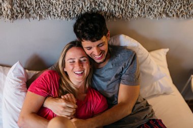 Yatakta gülümseyen, kucaklayan gelin ve damadın üst görüntüsü. Tatil