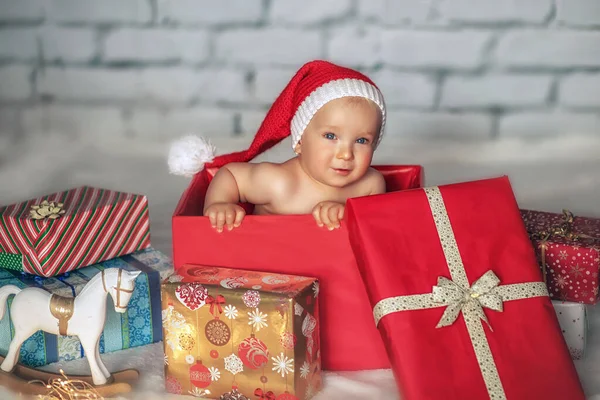 戴着圣诞礼帽的可爱小男孩坐在礼品盒里 圣诞节的概念 — 图库照片