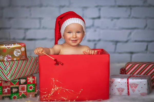 戴着圣诞礼帽的可爱小男孩坐在礼品盒里 圣诞节的概念 — 图库照片