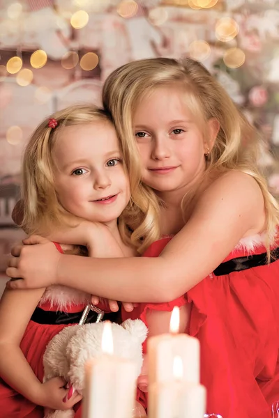 Duas meninas alegres bonitos em roupas de Natal contra o fundo da árvore de Natal — Fotografia de Stock