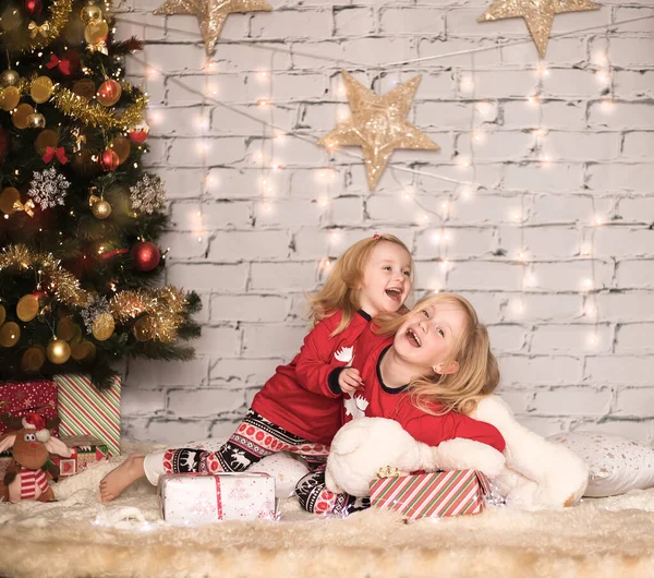 Duas meninas alegres bonitos em roupas de Natal contra o fundo da árvore de Natal — Fotografia de Stock