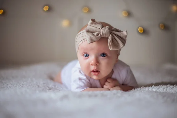 Menina bebê 3 meses de idade encontra-se em uma cama com roupas brancas em seu estômago, bebê de manhã, conceito de coisas de bebê — Fotografia de Stock