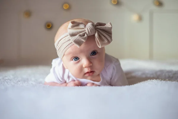 Menina bebê 3 meses de idade encontra-se em uma cama com roupas brancas no estômago e sorri, olha para a câmera, bebê de manhã, conceito de coisas de bebê — Fotografia de Stock