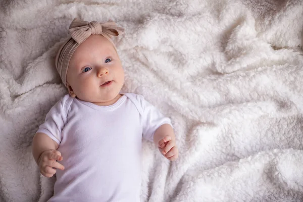 小女孩躺在白色的毛毯上 穿着白色的衣服 面带微笑 看着相机 婴儿的早晨 婴儿的概念 案文的位置 — 图库照片