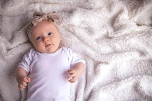 Bebek kız, beyaz bir battaniyenin üzerinde karnının üzerinde uzanıyor ve gülümsüyor, kameraya bakıyor, bebek eşyası konsepti. metin için yer.
