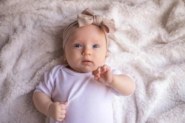 小女孩躺在白色的毛毯上 穿着白色的衣服 面带微笑 看着相机 婴儿的早晨 婴儿的概念 案文的位置 — 图库照片