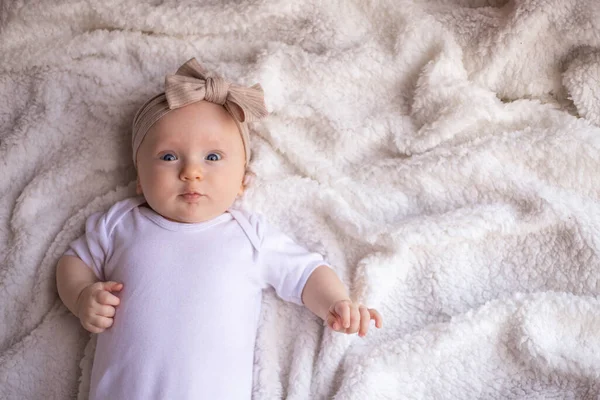 Bebek kız, beyaz bir battaniyenin üzerinde karnının üzerinde uzanıyor ve gülümsüyor, kameraya bakıyor, bebek eşyası konsepti. metin için yer.